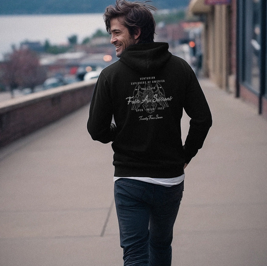 Man wearing a black hoodie with text on the back, standing on a sidewalk.