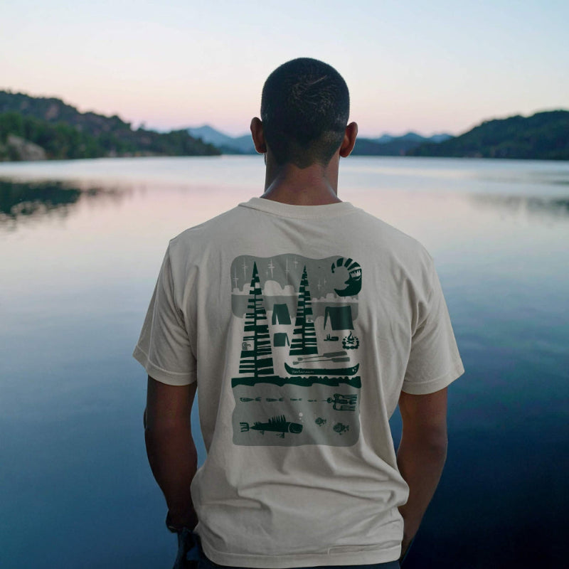 Person wearing a t-shirt with a nature graphic, standing by a lake at sunset.