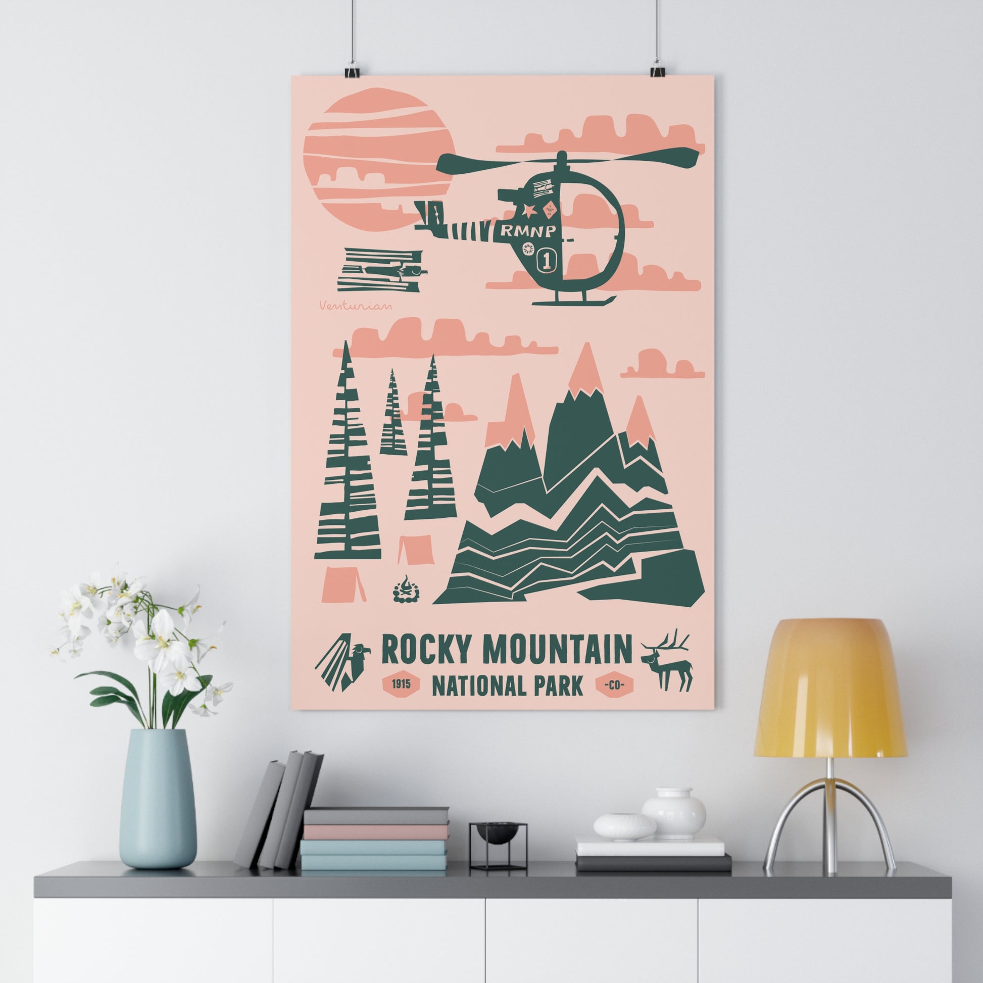 Poster of Rocky Mountain National Park with a helicopter and mountain design on a pink background, displayed on a wall above a shelf.