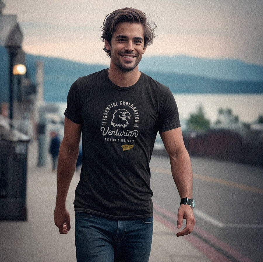 Man wearing a black t-shirt with a logo and text, standing outdoors with a scenic background.