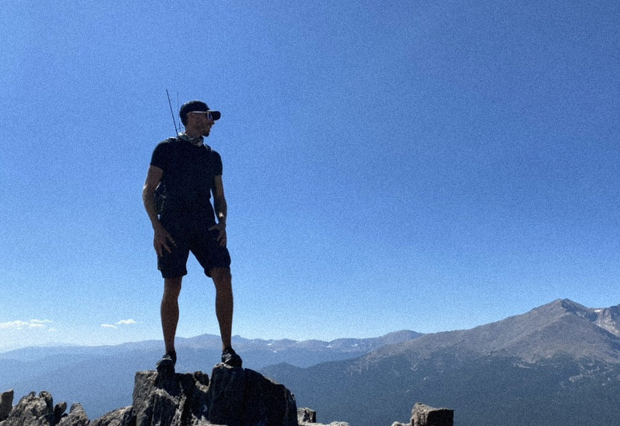 Person standing on a rocky outcrop with mountains and clear blue sky in the background