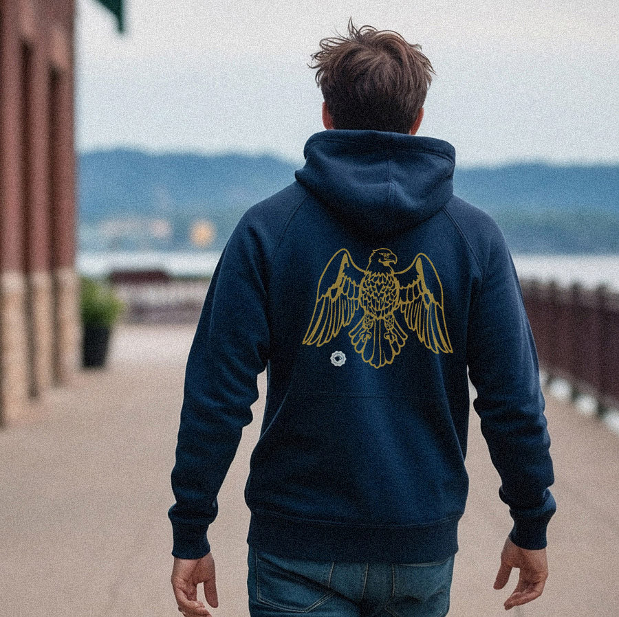 Person wearing a navy hoodie with a gold eagle design, standing outdoors.